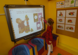 Dziewczynka rozwiązuje quiz na tablicy interaktywnej, wskaźnik unosi w kierunku właściwej odpowiedzi.