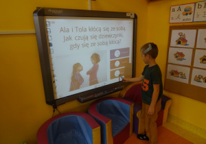 Chłopiec rozwiązuje quiz na tablicy interaktywnej, wskaźnik unosi w kierunku właściwej odpowiedzi.