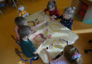 Piątka dzieci maluje na folii buźkę z emocjami.