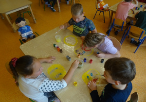Czwórka dzieci maluje na folii buźkę z emocjami.