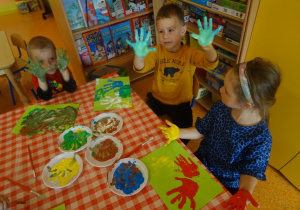 Dzieci mają uniesione rączki pomalowane farbą.