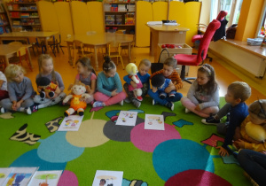 Dzieci siedzą w kole z lalkami, przed nimi rozłożone są ilustrację.