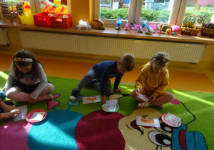 Trójka dzieci siedzi na dywanie, każdy układa obrazek z części.