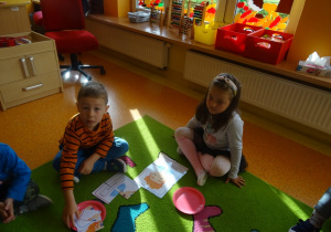 Dwójka dzieci układa na dywanie obrazek z części.