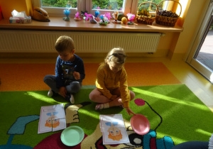 Dwójka dzieci układa na dywanie obrazek z części.