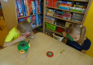 Dwoje dzieci ogląda przez lupy liście przy stoliku.