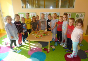 Grupa dzieci stoi wokół stolika na którym ułożone są półmiski z przygotowanymi szaszłykami owocowo- warzywnymi.