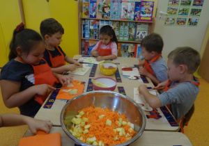 Pięcioro dzieci przy stole, przed każdym z dzieci leżą deski na których kroją owoce i warzywa.