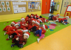 Grupa dzieci siedzi w małych grupach, przechylają się na boki, naśladują jazdę na sankach.