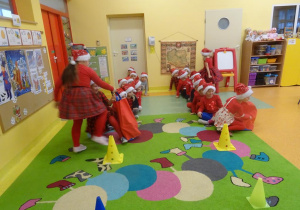 Dwie dziewczynki przekazują worki kolejnemu dziecku, w tle dzieci siedzą w dwóch rzędach.
