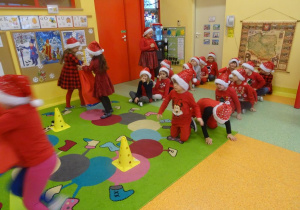 Dziewczynka przekazuje worek kolejnemu dziecku , w tle dzieci siedzą w dwóch rzędach.