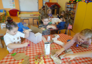 Troje dzieci przygotowuje stroje ekologiczne z papierowych rolek, worków plastikowych, sznurków.