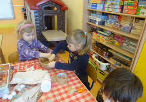 Dwie dziewczynki doklejają sznurek do papierowego pudełka.