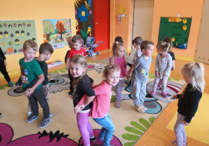 dzieci w parach stoją plecami do siebie na dywanie wykonując ćwiczenia