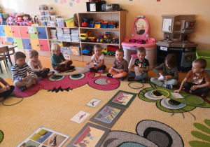 dzieci siedzą na dywanie po turecku przed każdym leży kolorowa obręcz, otwierają koperty