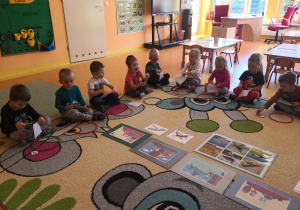 dzieci siedzą na dywanie po turecku przed każdym leży kolorowa obręcz, otwierają koperty