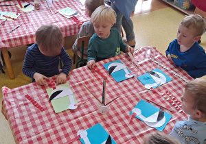 dzieci przy stolikach przyklejają przygotowane przez nauczyciela elementy bociana (tułów, szyja, głowa, dziób, długie czerwone nogi)