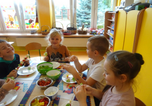 dzieci przy stolikach nadziewają na patyczki warzywa, nabiał tworząc szaszłyki