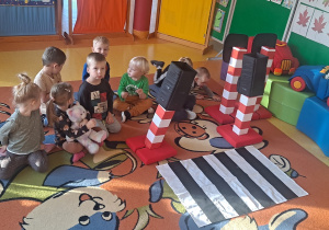 dzieci grzecznie czekają siedzą na dywanie na zajęcia przygotowane z bezpiecznego przechodzenia przez pasy