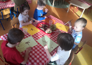 dzieci przy stolikach otrzymały na kartkach ilustrację baletnicy oraz zasuszone liście oraz kwiaty, smarują klejem kartkę i naklejają dary jesieni w miejsce spódnicy