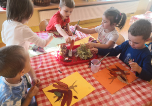 dzieci przy stolikach otrzymały na kartkach ilustrację baletnicy oraz zasuszone liście oraz kwiaty, smarują klejem kartkę i naklejają dary jesieni w miejsce spódnicy