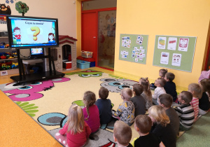 dzieci siedzą na dywanie i zainteresowaniem oglądają film edukacyjny o Polsce