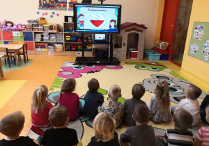 dzieci siedzą na dywanie i zainteresowaniem oglądają film edukacyjny o Polsce