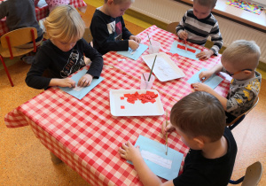 dzieci na przygotowanych kartkach wyklejają z czerwonych kwadracików flagę Polski