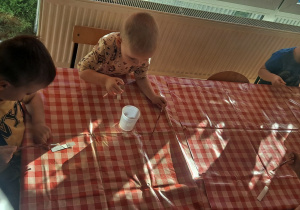dzieci przy stolikach smarują klejem tekturę