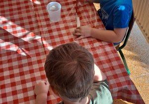 dzieci przy stolikach smarują klejem tekturę