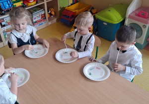 dzieci przy stolikach za pomocą słomki przenoszą kolorowe misie i układają je na talerzyku na odpowiednim kolorze