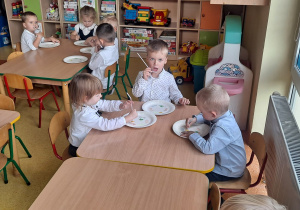 dzieci przy stolikach za pomocą słomki przenoszą kolorowe misie i układają je na talerzyku na odpowiednim kolorze