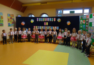dzieci stoją na tle ilustracji z okazji pasowania na przedszkolaka grupy najmłodszej