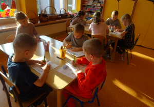 dzieci przy stolikach wykonują karty pracy