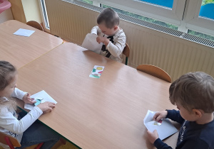 dzieci przy stolikach wyciągają z kopert przygotowane puzzle i je układają