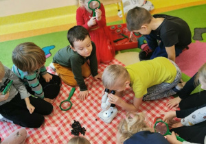 dzieci na dywanie na ceracie oglądają jak wygląda węgiel przy pomocy lup i mikroskopu