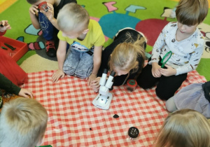 dzieci na dywanie na ceracie oglądają jak wygląda węgiel przy pomocy lup i mikroskopu