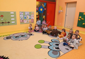 dzieci siedzą na dywanie w ulubionym misiem - maskotką na dywanie