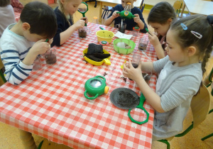 dzieci za pomocą lup oglądają uważnie węgiel