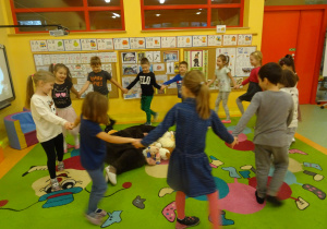 dzieci tańczą w koło pluszowych misi oraz przebranego nauczyciela śpiewając piosenkę "Stary niedźwiedź"
