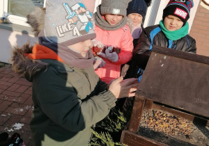 dzieci dosypują nasiona dla ptaków w karmniki