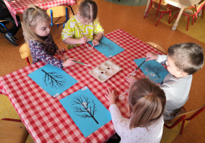 dzieci przy stolikach malują folię bąbelkową i odbijają ją na kartce z suchym drzewem