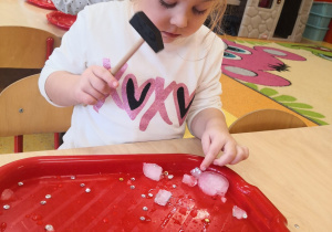 dzieci przy stolikach rozbijają kostki lodu i wyciągają zamarznięte skarby
