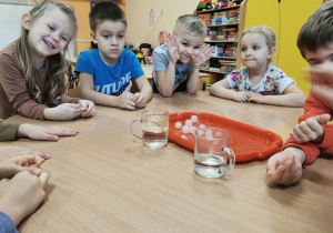 dzieci przy stoliku biorą kostkę lodu do ręki i sprawdzają jak się będzie ona zachowywać pod wpływem ciepła dłoni