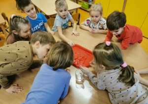 dzieci przy stoliku biorą kostkę lodu do ręki i sprawdzają jak się będzie ona zachowywać pod wpływem ciepła dłoni