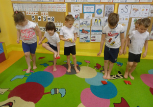 dzieci na dywanie przenoszą palcami od stóp woreczki