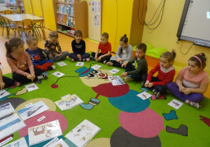 dzieci siedzą na dywanie i oglądają ilustracje