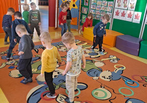 dzieci przeskakują nad szarfami obunóż i przechodzą przez tor stawiając stopy w wyznaczone miejsca, utrzymują równowagę przechodząc pro woreczkach