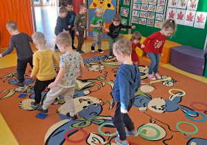 dzieci przeskakują nad szarfami obunóż i przechodzą przez tor stawiając stopy w wyznaczone miejsca, utrzymują równowagę przechodząc pro woreczkach