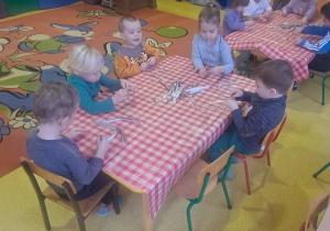 dzieci przy stolikach drą paski z gazet na mniejsze kawałeczki